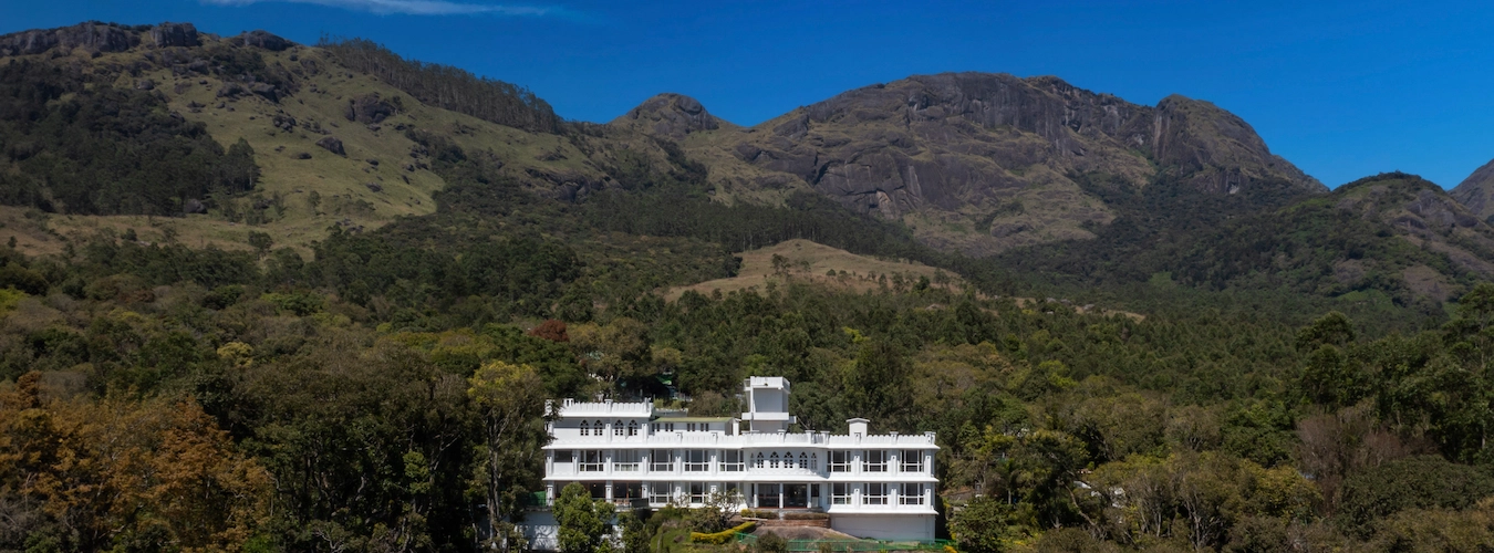 Exterior view of Fort Munnar resort building surrounded by lush green hills in Chinnakanal