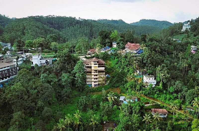 Aerial drone view of Misty Dale Munnar Resort And Spa surrounded by lush green hills in Anachal