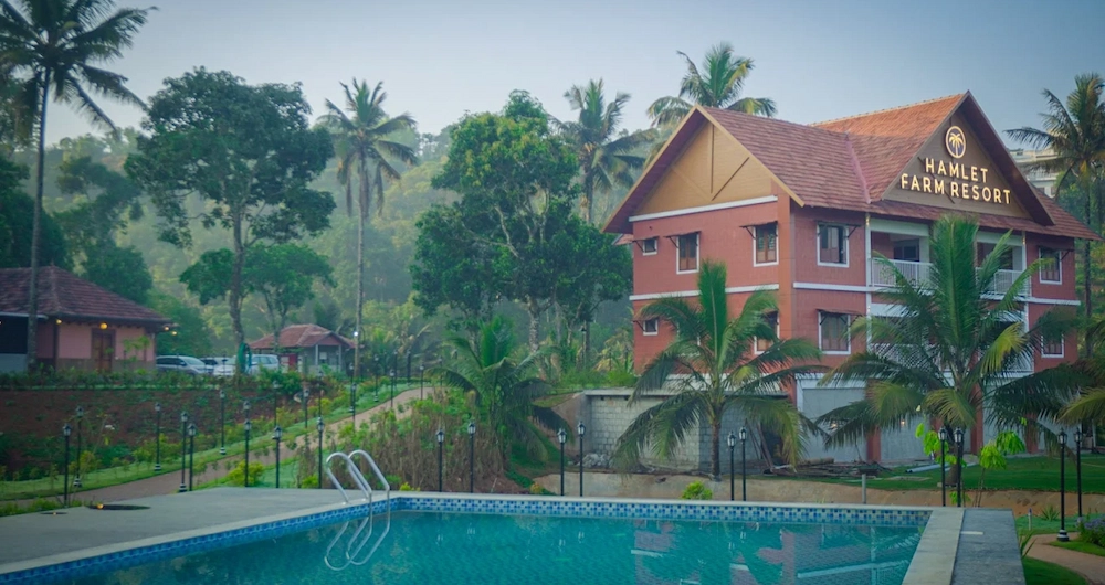 Resort building with red tile roof overlooking an outdoor swimming pool at The Hamlet Farmstead Munnar