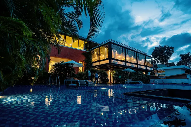 Night view of the illuminated luxury resort building and outdoor pool deck at The Leaf Munnar