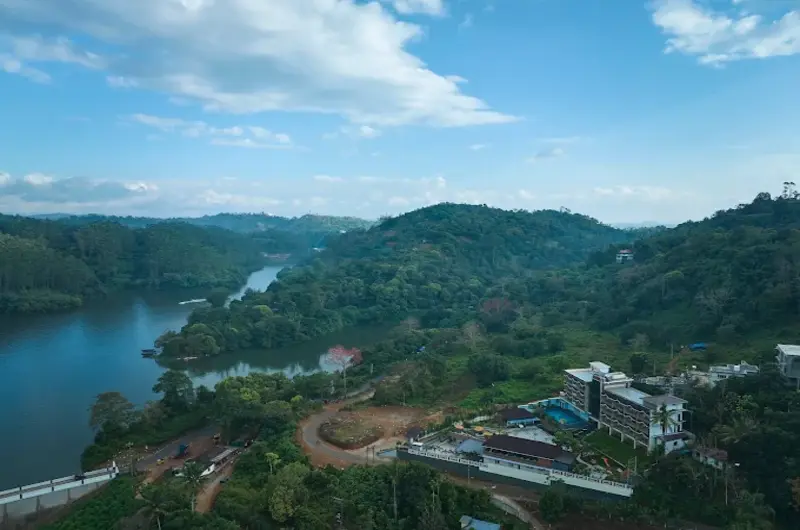 Scenic aerial drone view of the lush green mountains and winding river surrounding Eve Munnar Luxury Resort