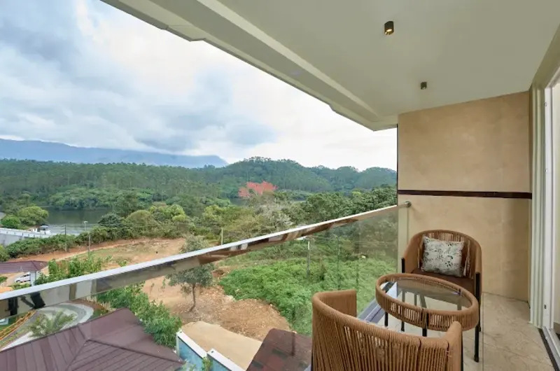 Private resort balcony with outdoor seating and a stunning view of the misty valley at Eve Munnar Luxury Resort