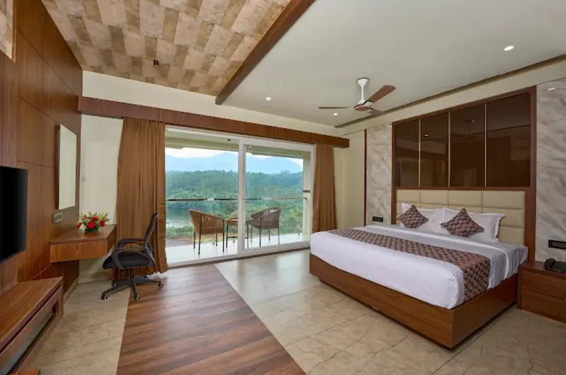 Premium resort bedroom featuring a large glass window with a panoramic mountain view at Eve Munnar Luxury Resort