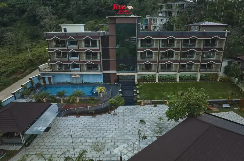 Daytime exterior facade of Eve Munnar Luxury Resort building featuring an outdoor pool and green hills
