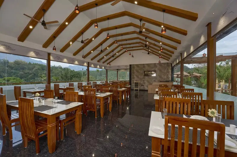Spacious resort restaurant with wooden dining tables and large windows overlooking Eve Munnar Luxury Resort grounds