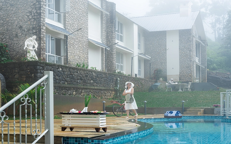 Outdoor swimming pool with sun loungers at 1924 Clock House Resort Munnar