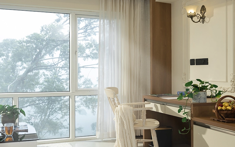 Guest room with large window overlooking green gardens at 1924 Clock House Resort Munnar