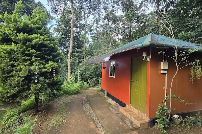 Cozy brick cottage exterior nestled among trees at Pepper County Farm Stay Munnar