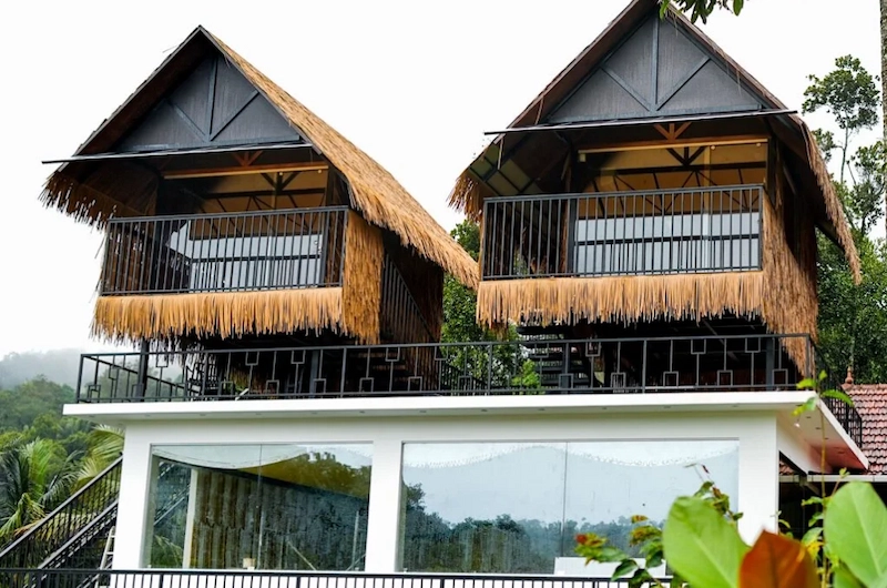 Elevated wooden eco-cottages with balcony view surrounded by forest trees at The Hamlet Farmstead Munnar