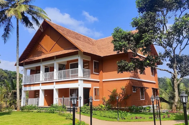 Two-story brick resort villa with spacious balcony and palm trees at The Hamlet Farmstead Munnar