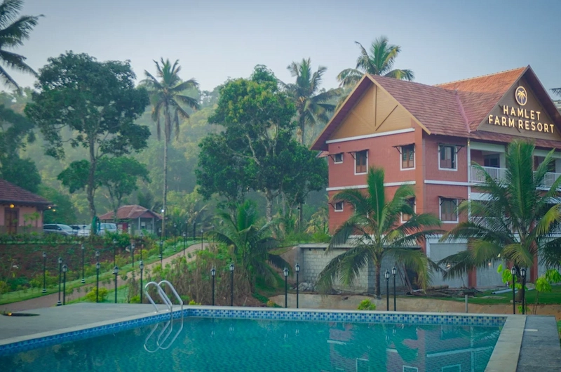 Resort building with red tile roof overlooking outdoor swimming pool at The Hamlet Farmstead Munnar