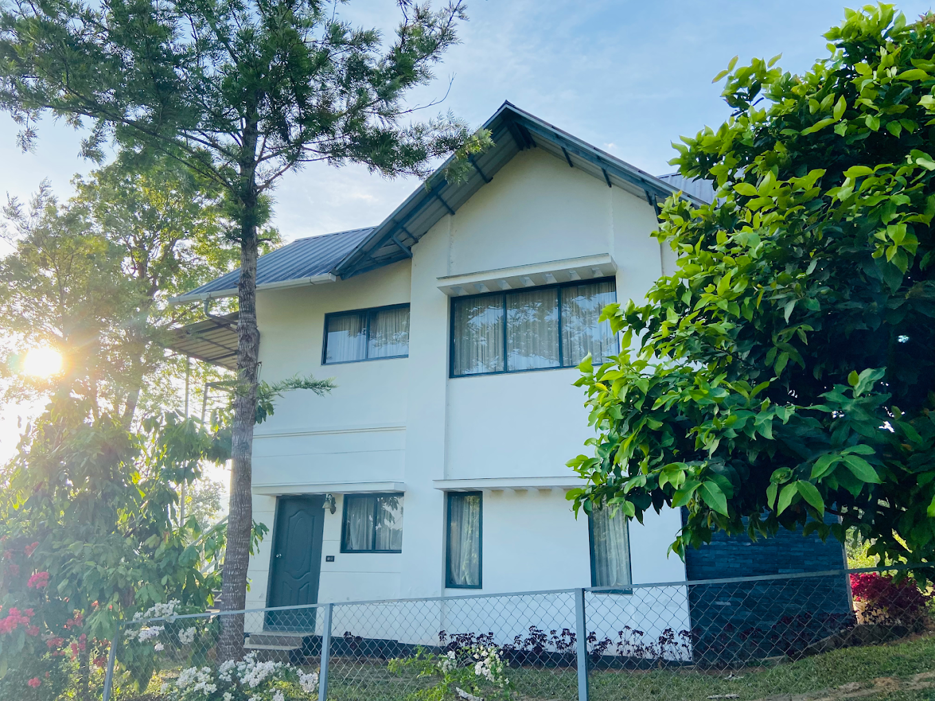 Modern farmstay building surrounded by green trees under sunny sky at Mannoor Farmstay Munnar