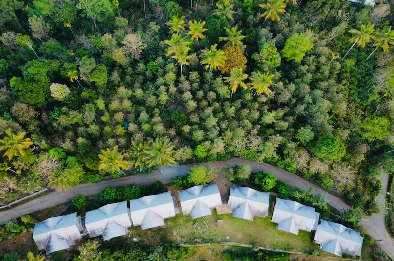 Aerial view of Mannoor Farmstay resort buildings surrounded by lush green hills in Munnar