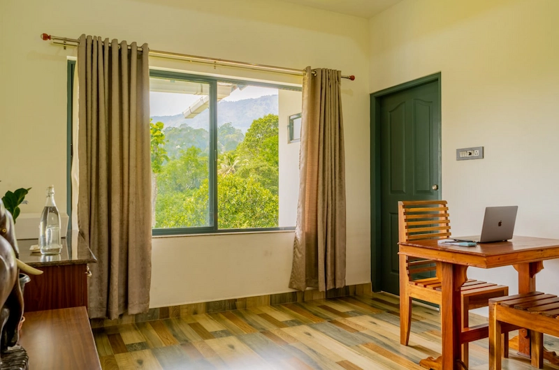 Cozy resort bedroom with large window offering scenic green mountain views in Munnar