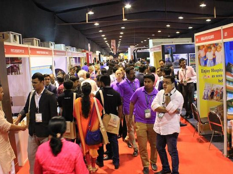 Exhibitors and visitors discussing tourism packages at Kerala Travel Mart stall in Kochi