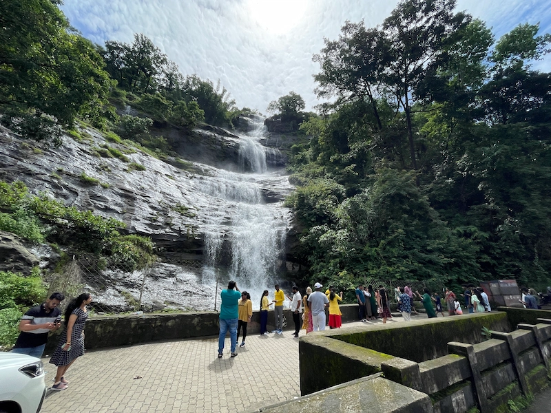 Tourist walking near scenic waterfall cascading over rocks in green hills of Munnar